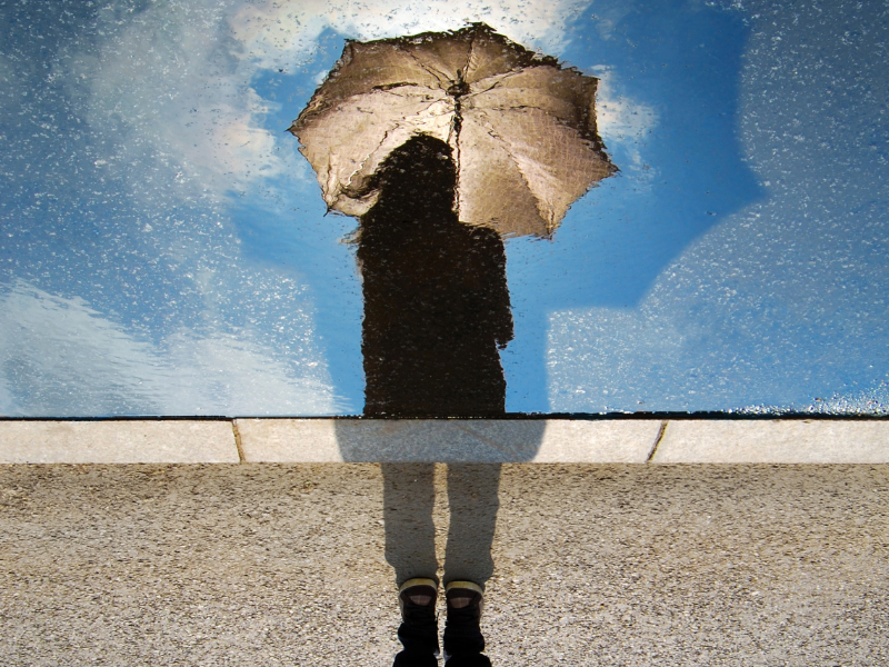 Person with umbrella reflected in a puddle
